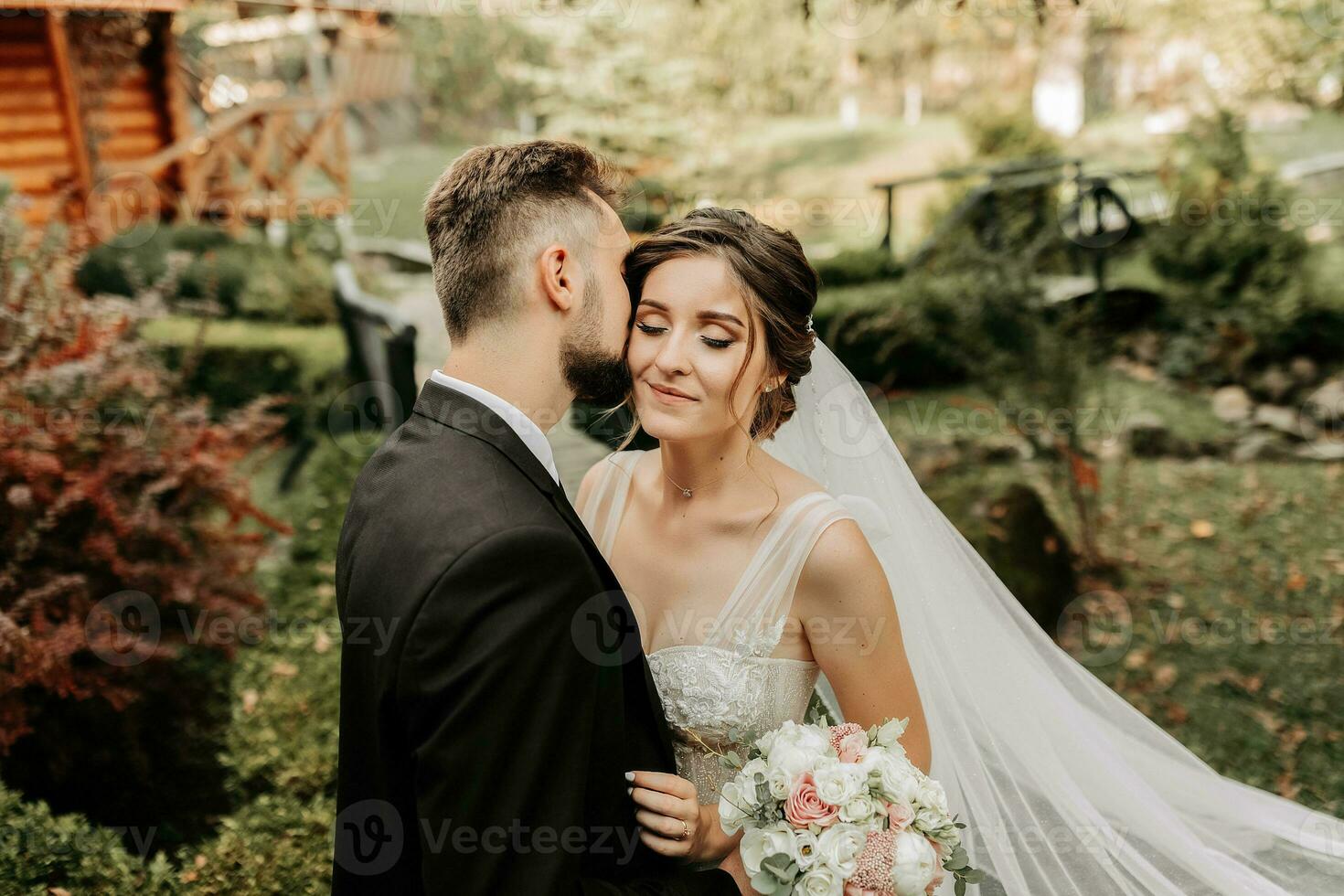 maravilloso elegante lujoso novia con velo soplo en el viento. y un elegante novio Beso al aire libre cerca alto otoño arboles foto