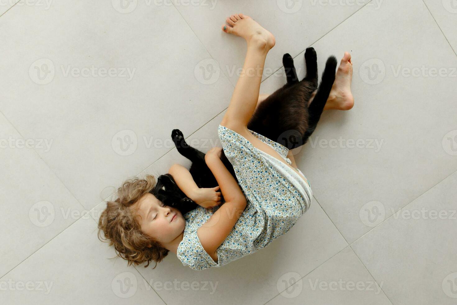 A happy child is lying on the veranda with his favorite black cat. A little girl rests on the floor of the veranda on a sunny summer day. A happy and carefree childhood. photo