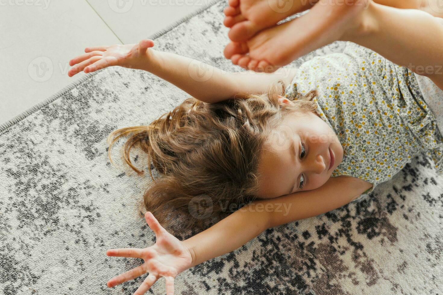 A happy child lies on the background of a modern carpet on the veranda. A little girl rests on the floor of the veranda on a sunny summer day photo