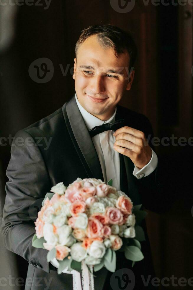 Preparation for the morning of the bride and groom. portrait photo of an elegant man getting dressed for a wedding celebration. The groom, dressed in a white shirt, bow tie and jacket