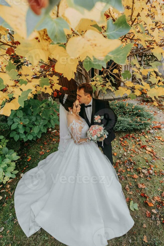 Groom and bride in autumn forest, wedding ceremony, side view. Groom and bride on the background of yellowed autumn leaves. The photo was taken through the yellowing leaves of the trees