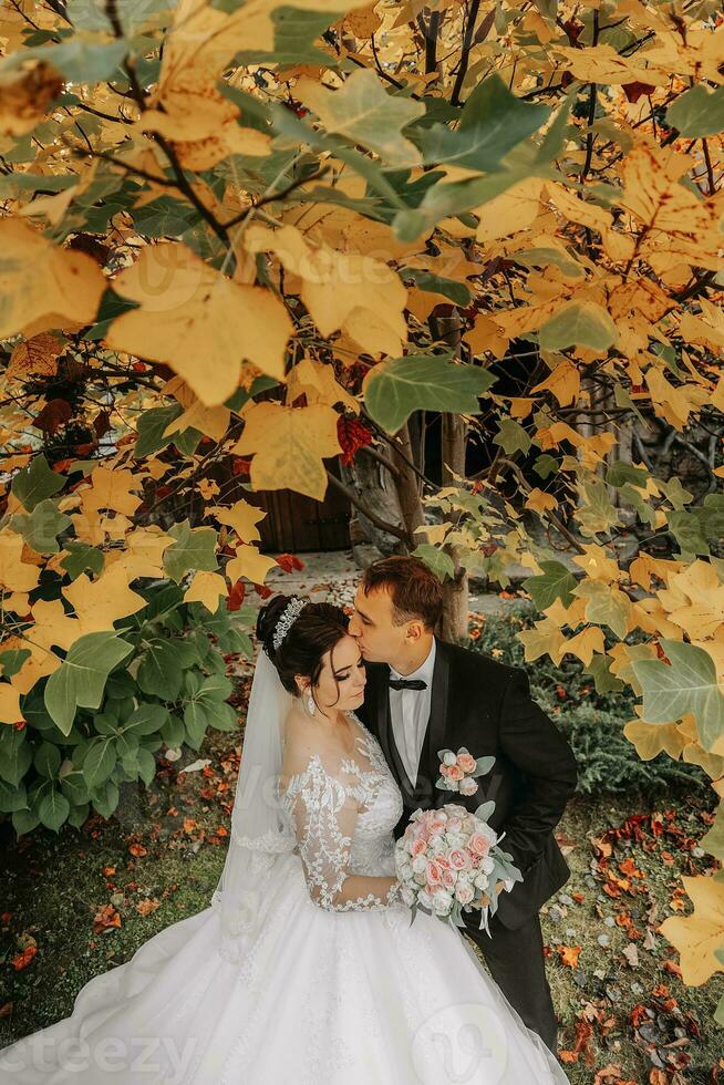 Groom and bride in autumn forest, wedding ceremony, side view. Groom and bride on the background of yellowed autumn leaves. The photo was taken through the yellowing leaves of the trees