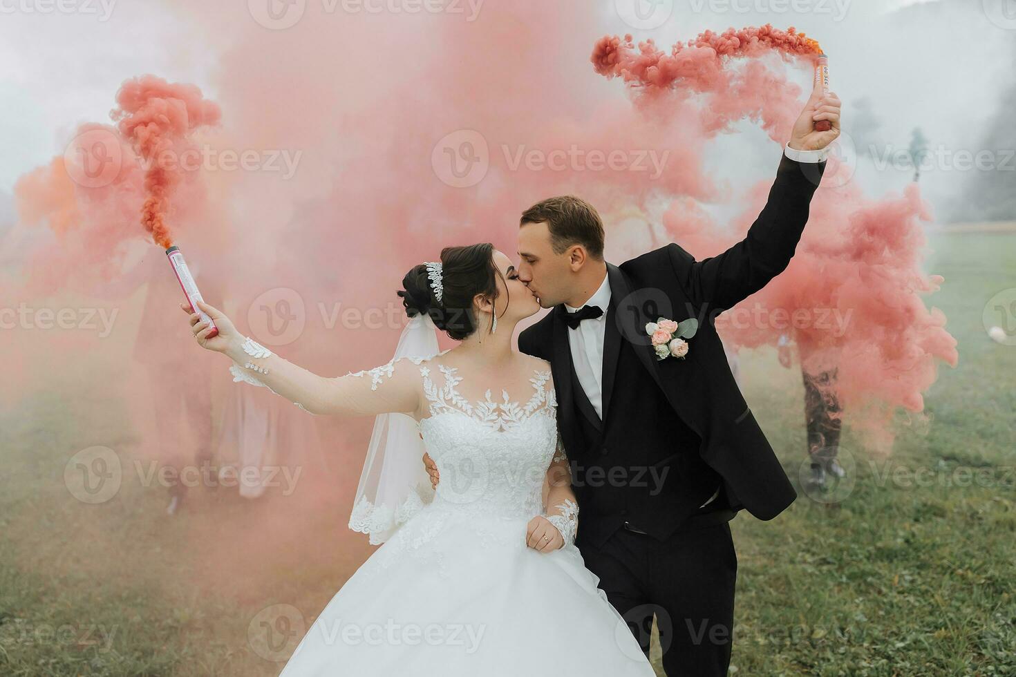 Beautiful newlyweds stand in a field against the background of mountains and hold multi-colored smoke bombs in their hands. Wedding photography. photo