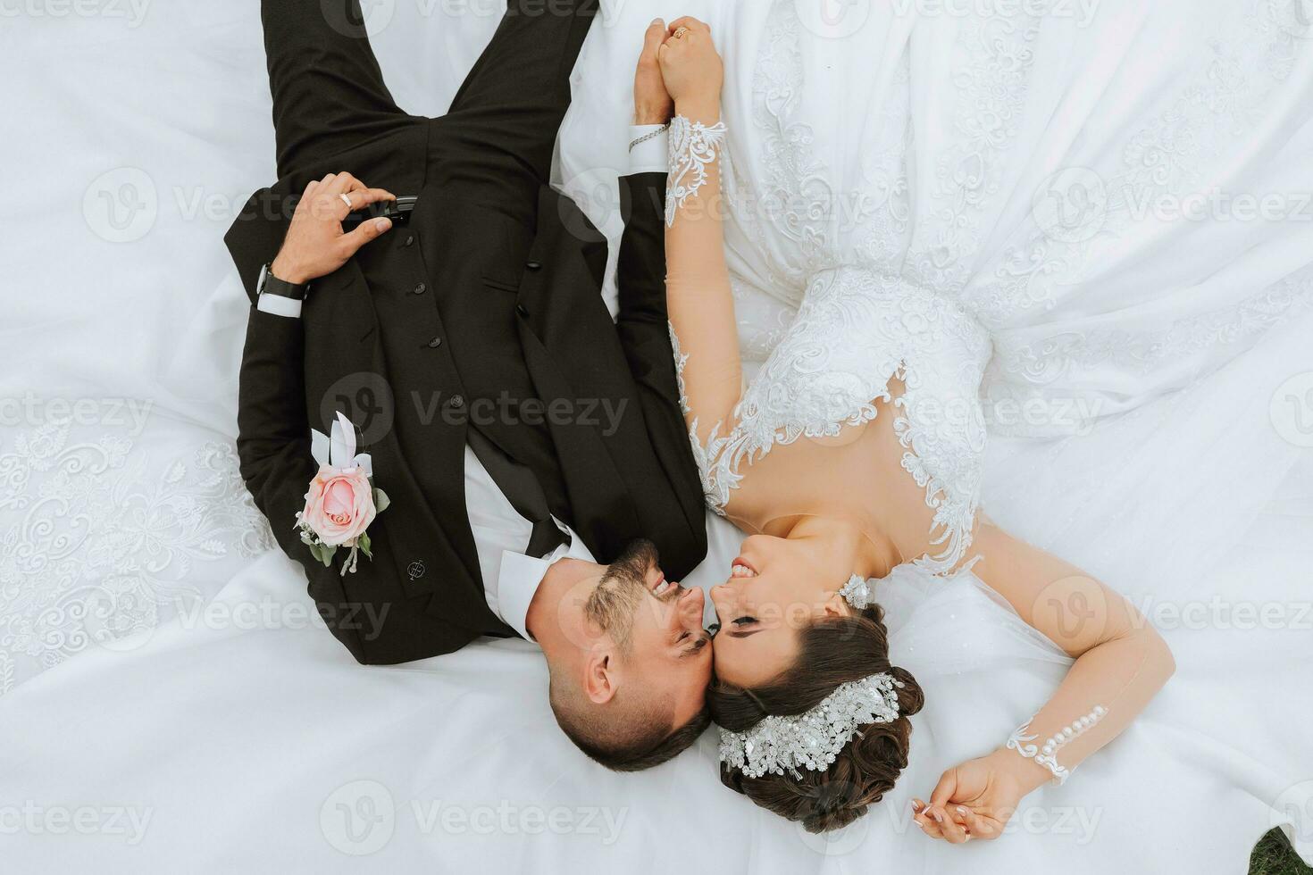 beautiful fairy tale happy bride and stylish groom lying on the grass on their wedding day photo