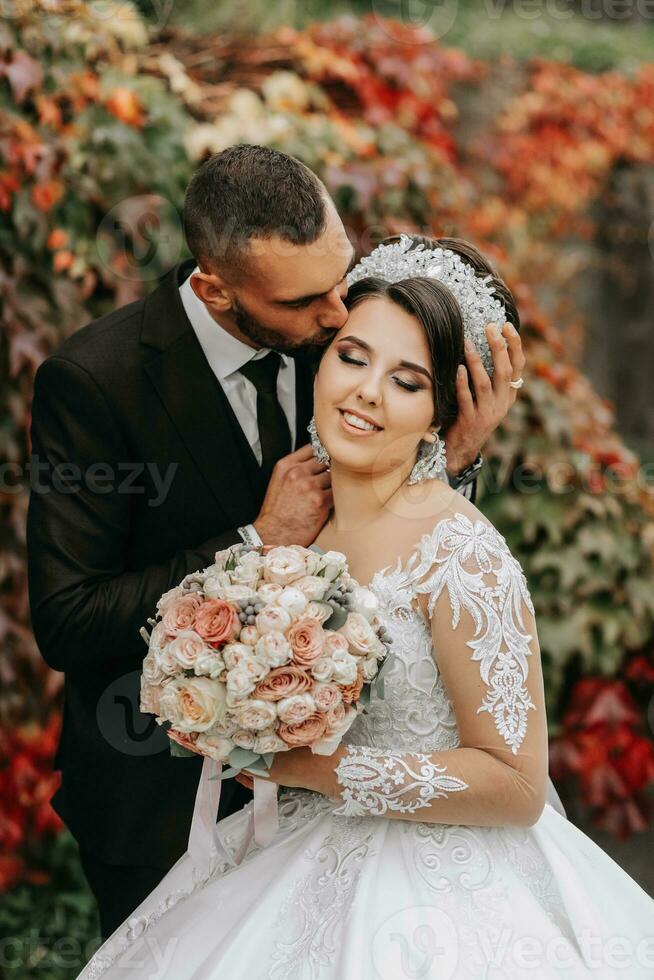 The bride and groom in the autumn park near the house, wedding ceremony, front view. Groom and bride on the background of yellowed autumn leaves. photo