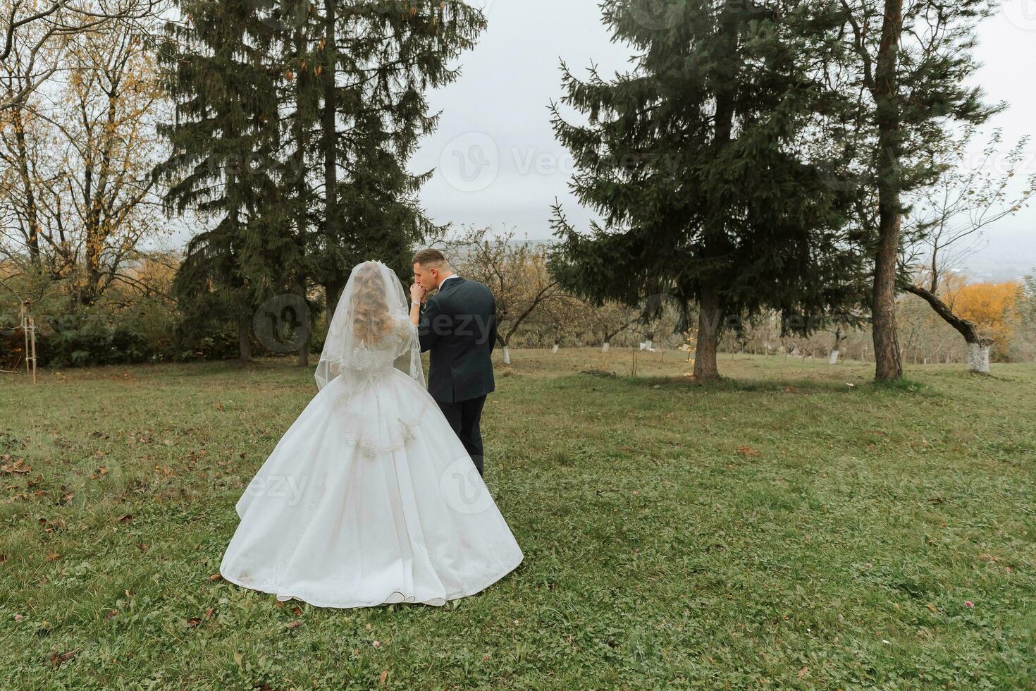 Happy stylish couple of newlyweds in the green forest on an autumn day. the bride in a classic long white dress and the groom in a blue suit embrace. wedding day. photo