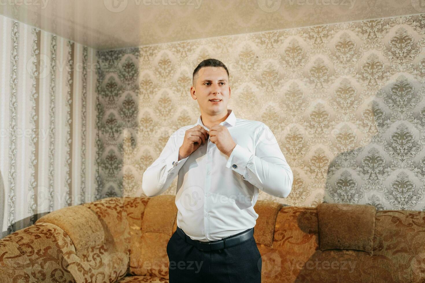 retrato de un hombre a hogar abotonarse su camisa. el novio es preparando para el boda. el hombre es vistiendo un blanco camisa. elegante novio foto