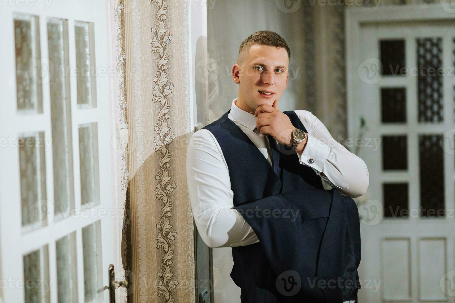 An elegant groom is holding a jacket on his arm in his room. Details of the wedding morning. Details Beauty and fashion. photo