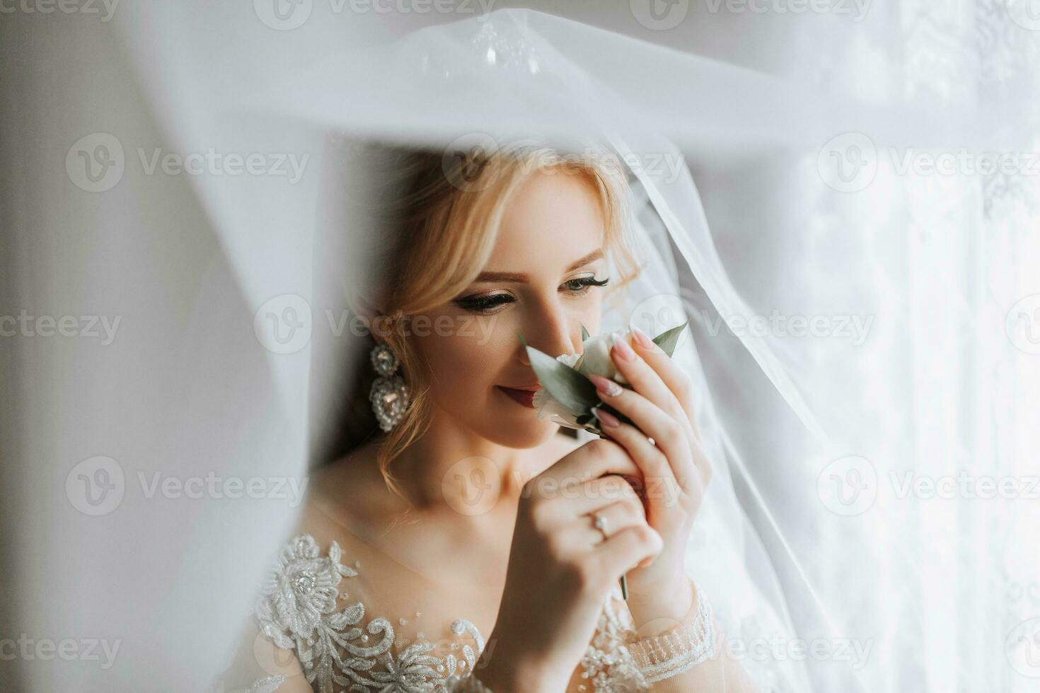 Happy beautiful bride under a veil close-up. Beautiful bride with professional makeup and hairstyle. The bride in a white dress plays with her veil. photo