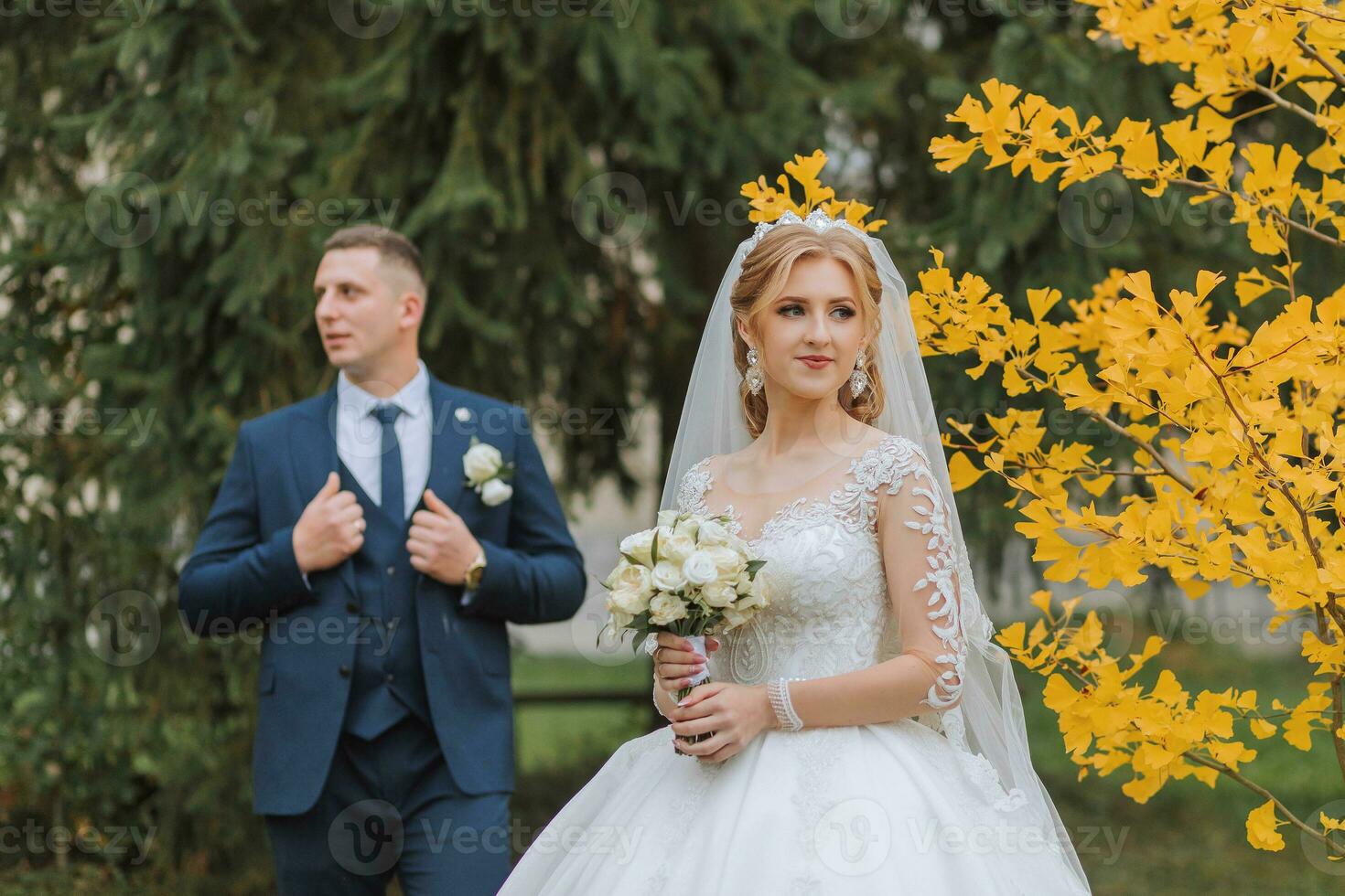 Groom and bride in autumn forest, wedding ceremony, side view. Groom and bride on the background of yellowed autumn leaves. The photo was taken through the yellowing leaves of the trees