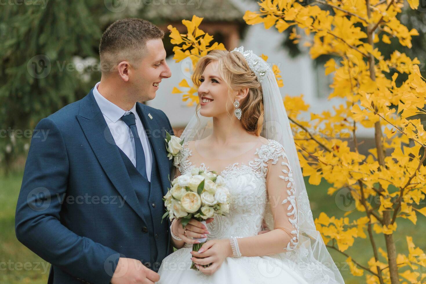 Groom and bride in autumn forest, wedding ceremony, side view. Groom and bride on the background of yellowed autumn leaves. The photo was taken through the yellowing leaves of the trees