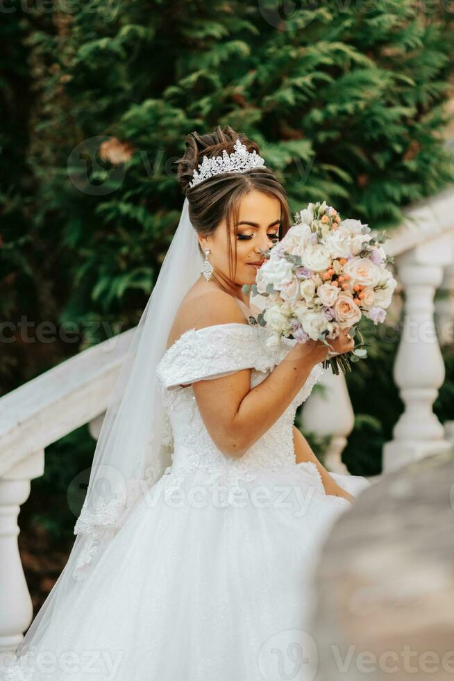 retrato de el novia en el otoño parque en Roca pasos. el novia en un Boda vestir en un natural antecedentes con un ramo de flores de flores en su manos. Boda día. foto
