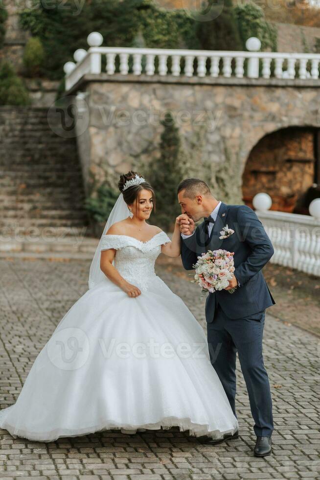 Gorgeous wedding couple walking on stone stairs near old castle in park. Stylish beautiful bride in amazing gown and groom posing on background of ancient building photo