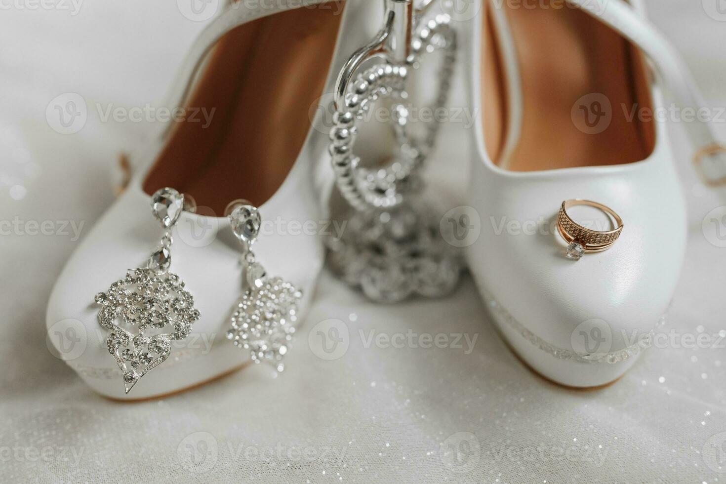 Wedding shoes of the bride with earrings and a gold wedding ring on the train of the wedding dress photo