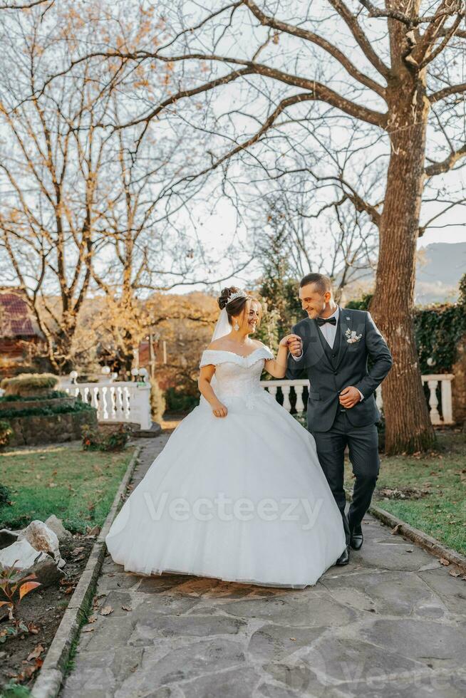 el novio sostiene el de la novia mano y camina. de el novia en contra el antecedentes de el del sol rayos, el parque y el bosque. foto