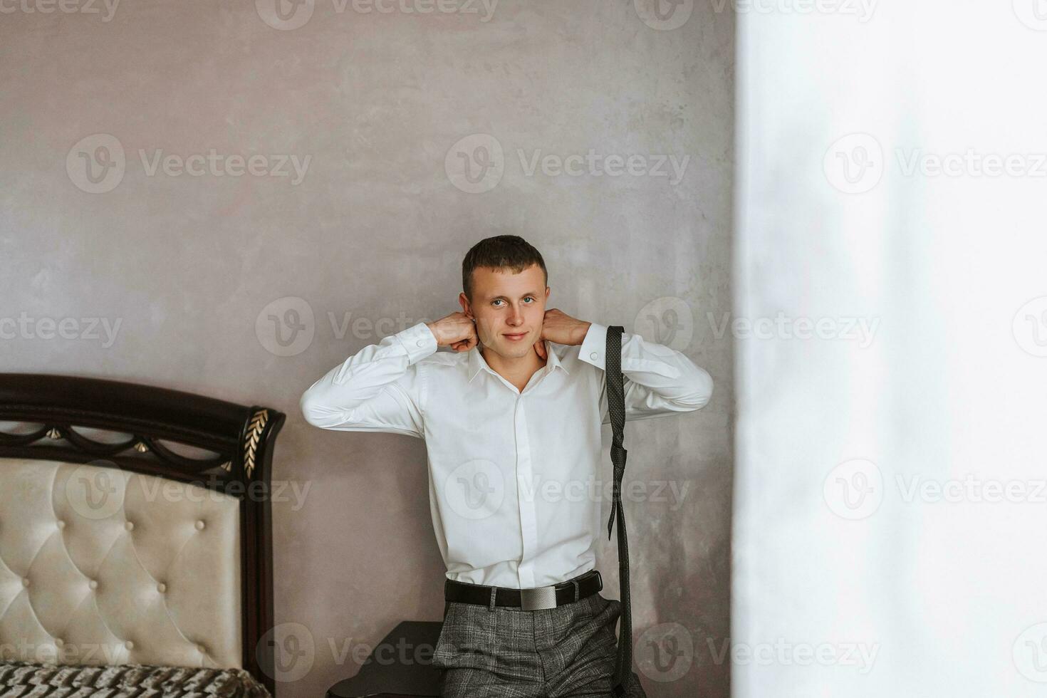 The groom puts on his tie in his room and prepares for the wedding. The man wears a tie photo