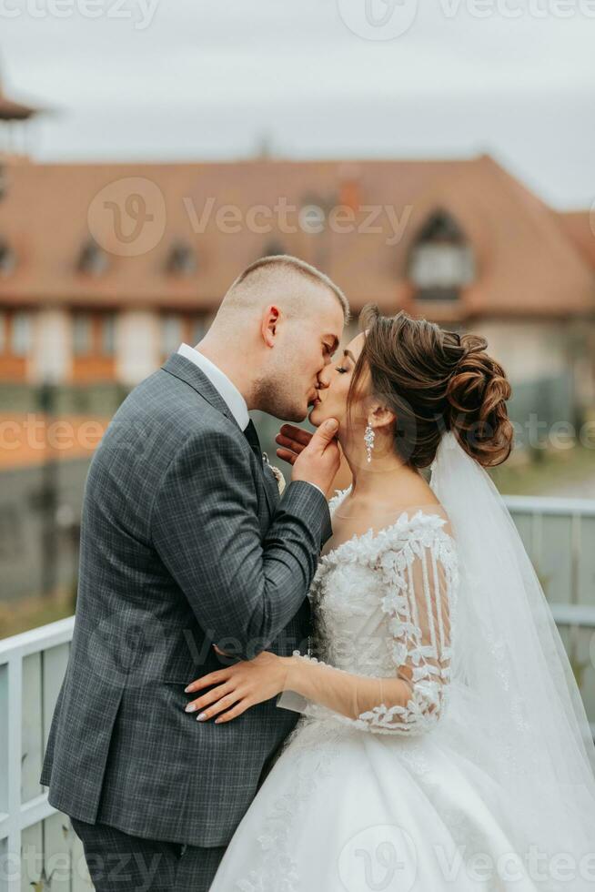 Stylish bride and groom tenderly embrace and kiss. Beautiful bride with modern bouquet embracing stylish groom in autumn park. Sensual romantic moment. Wedding. Stylish and beautiful. photo