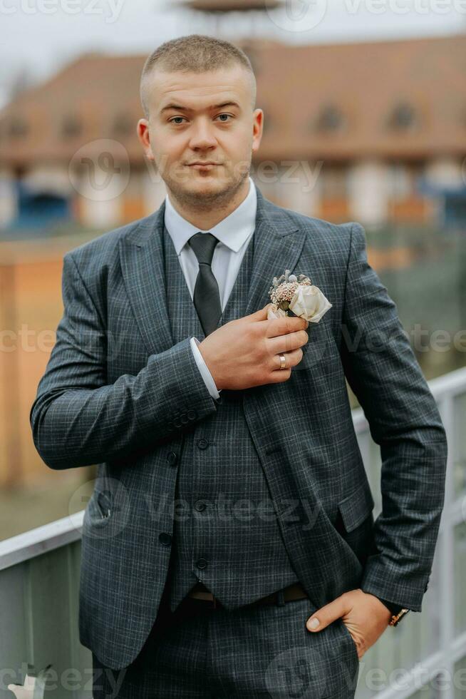 Handsome groom in suit and tie standing on balcony outdoors. Wedding portrait. A man in a classic suit photo