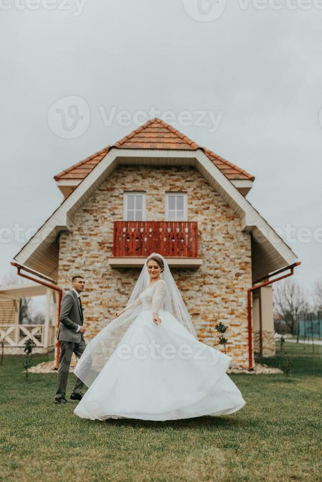 Groom and bride walking and holding hands in the park among tall green trees. Wide-angle autumn photo. Voluminous wedding dress. Classic suit of the groom photo