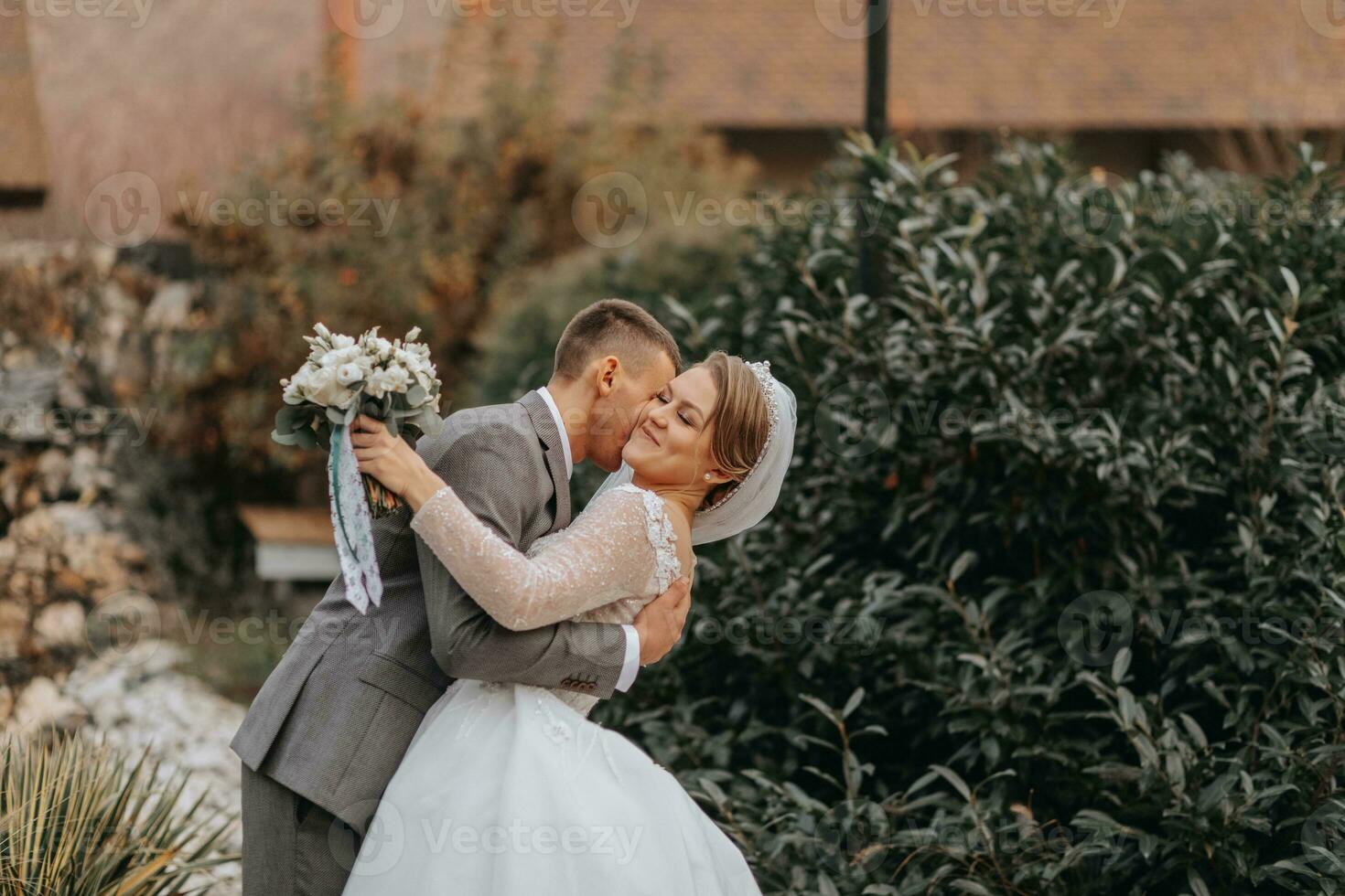 elegante novia y novio tiernamente abrazo y beso. hermosa novia con moderno ramo de flores abrazando elegante novio en otoño parque. sensual romántico momento. boda. elegante y hermosa. foto