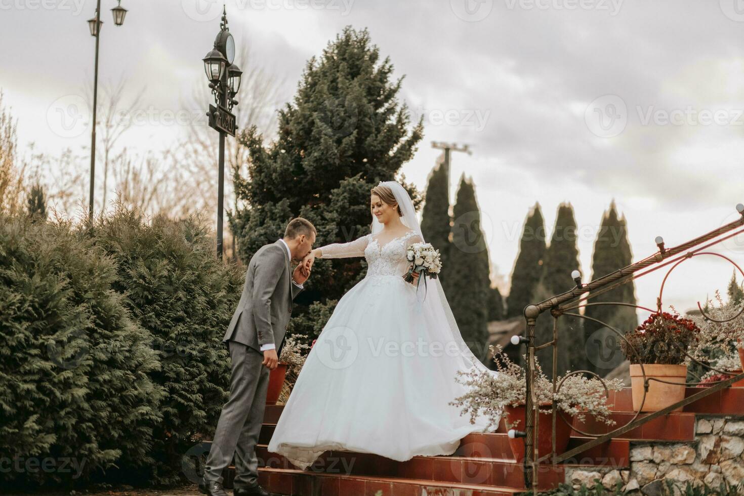 Stylish bride and groom tenderly embrace and kiss. Beautiful bride with modern bouquet embracing stylish groom in autumn park. Sensual romantic moment. Wedding. Stylish and beautiful. photo