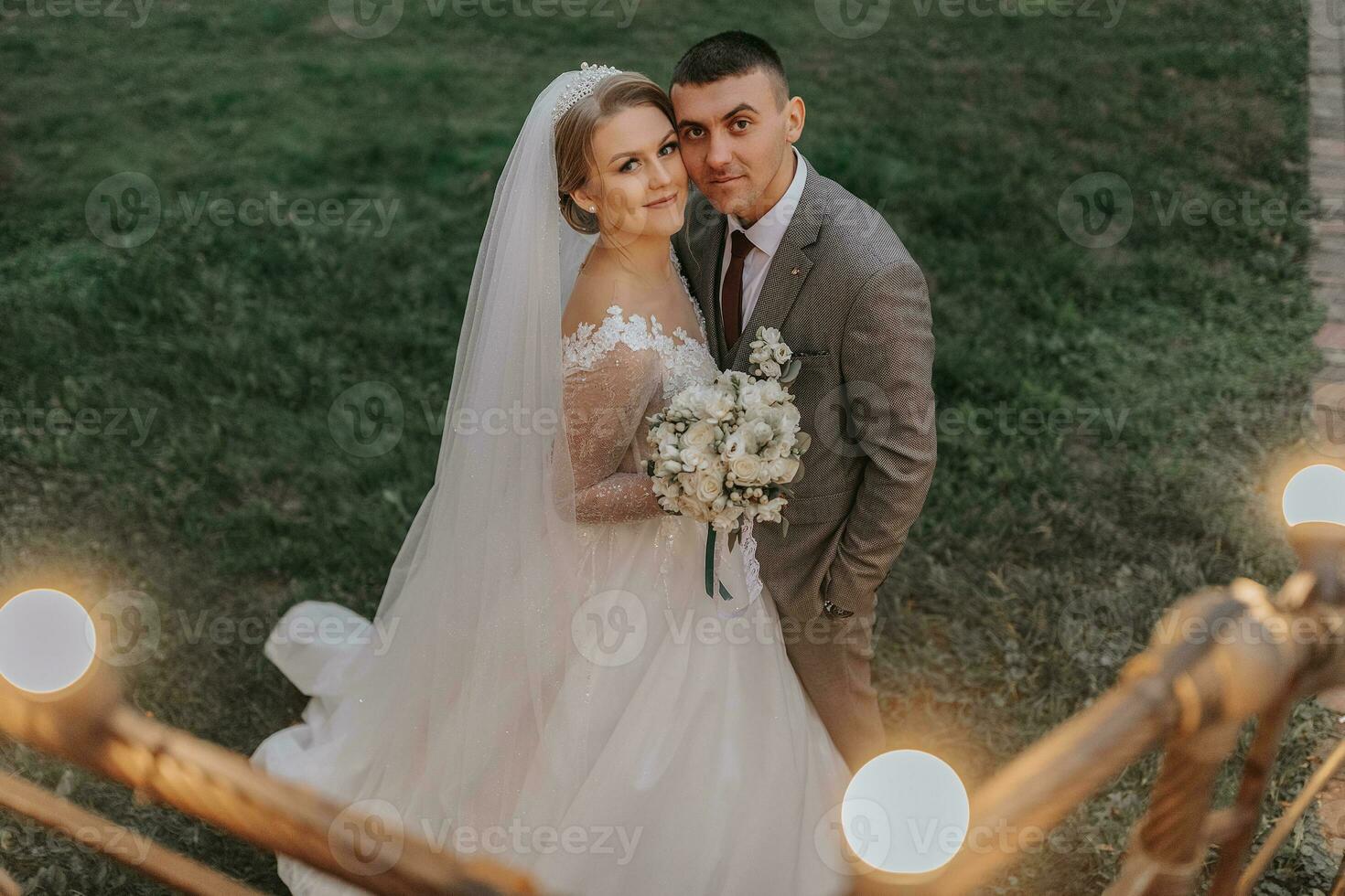 Stylish bride and groom tenderly embrace and kiss. Beautiful bride with modern bouquet embracing stylish groom in autumn park. Sensual romantic moment. Wedding. Stylish and beautiful. photo