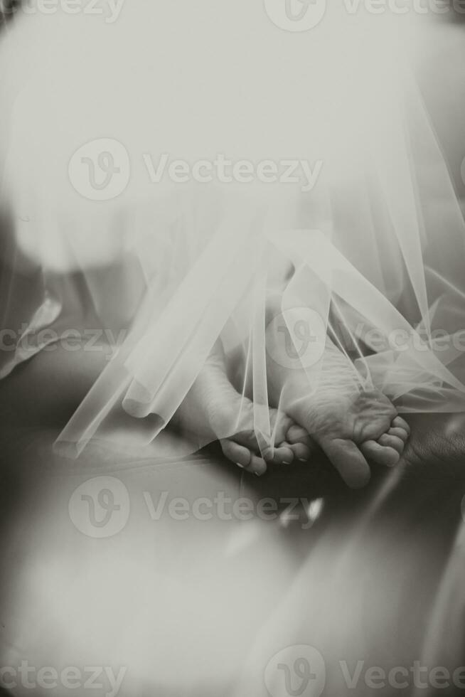 beautiful bare legs of the bride under veil lying on the bed. Black and white photo