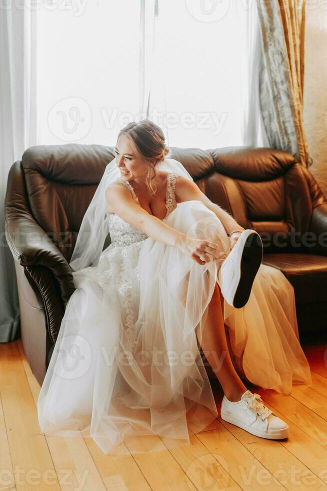 Happy bride wearing sneakers for wedding. Preparing the bride for the ceremony. Comfortable shoes for a wedding. White sneakers. photo