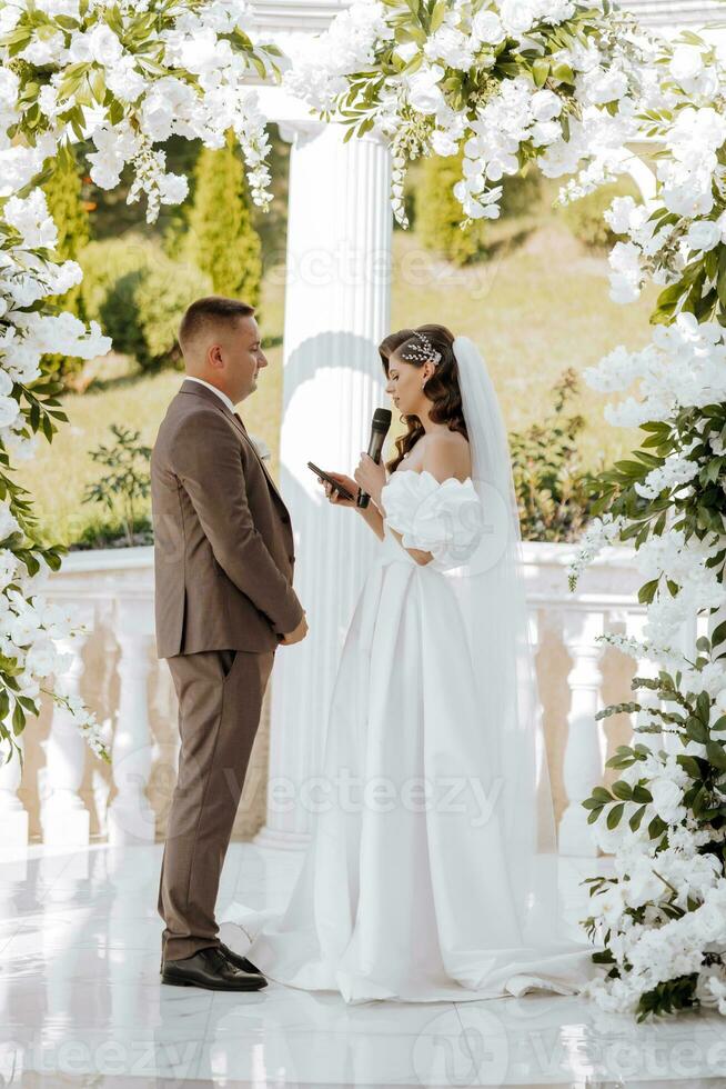 sensitive ceremony of the bride and groom. A happy newlywed couple is standing against the background of a wedding arch, she says yes to him. Wedding vows. The emotional part of the wedding photo