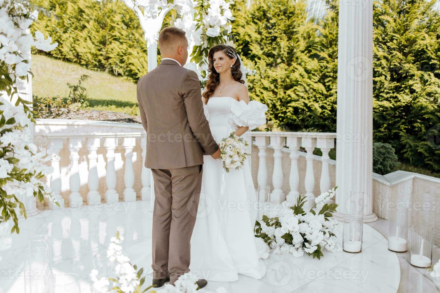 sensitive ceremony of the bride and groom. A happy newlywed couple is standing against the background of a wedding arch, she says yes to him. Wedding vows. The emotional part of the wedding photo