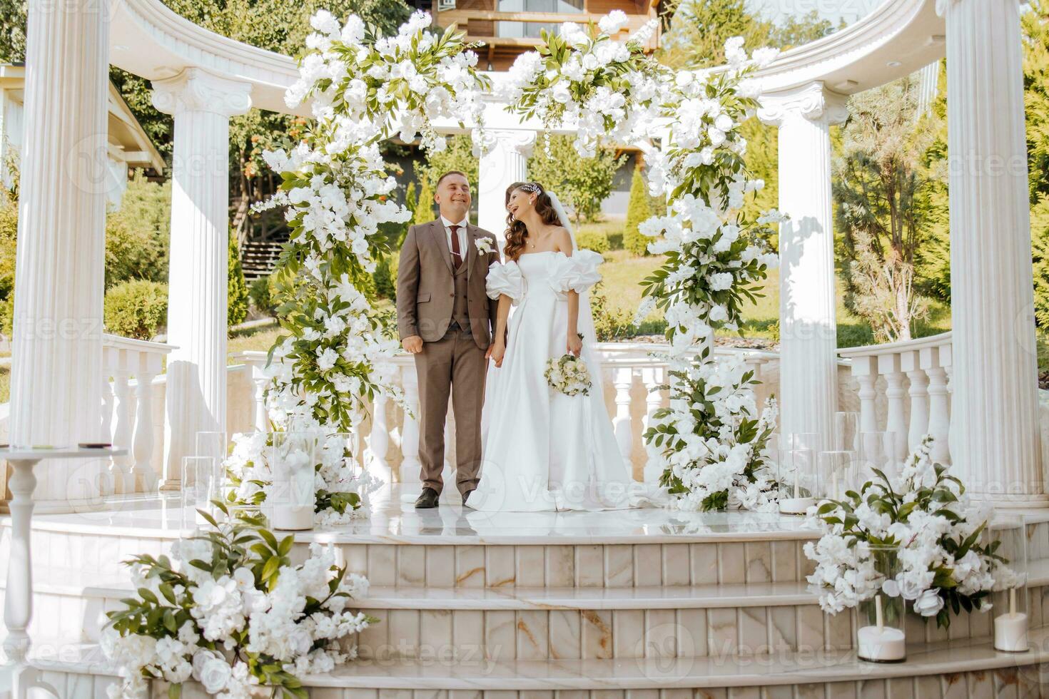 sensitive ceremony of the bride and groom. A happy newlywed couple stands against the background of a wedding arch decorated with fresh flowers photo
