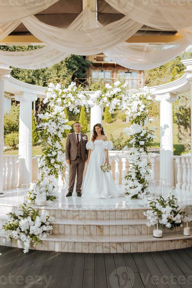 sensitive ceremony of the bride and groom. A happy newlywed couple stands against the background of a wedding arch decorated with fresh flowers photo