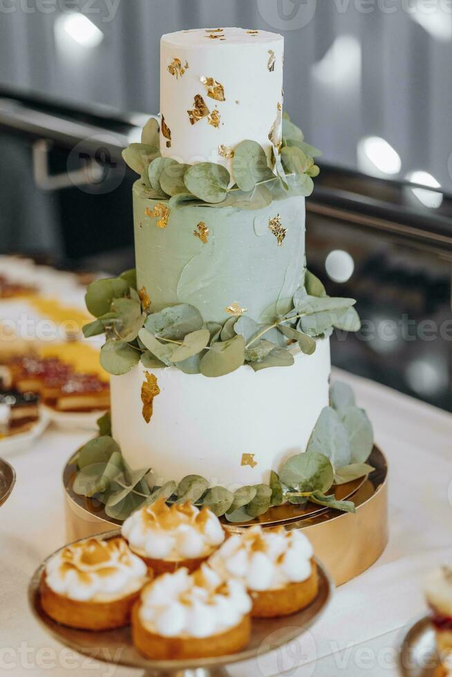 A three-tier mint-colored wedding cake decorated with green leaves and ashes stands on a table in a restaurant photo