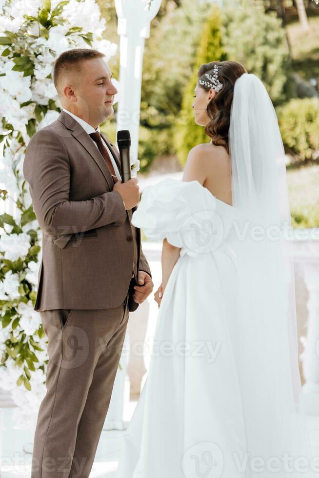 sensitive ceremony of the bride and groom. A happy newlywed couple is standing against the background of a wedding arch, she says yes to him. Wedding vows. The emotional part of the wedding photo