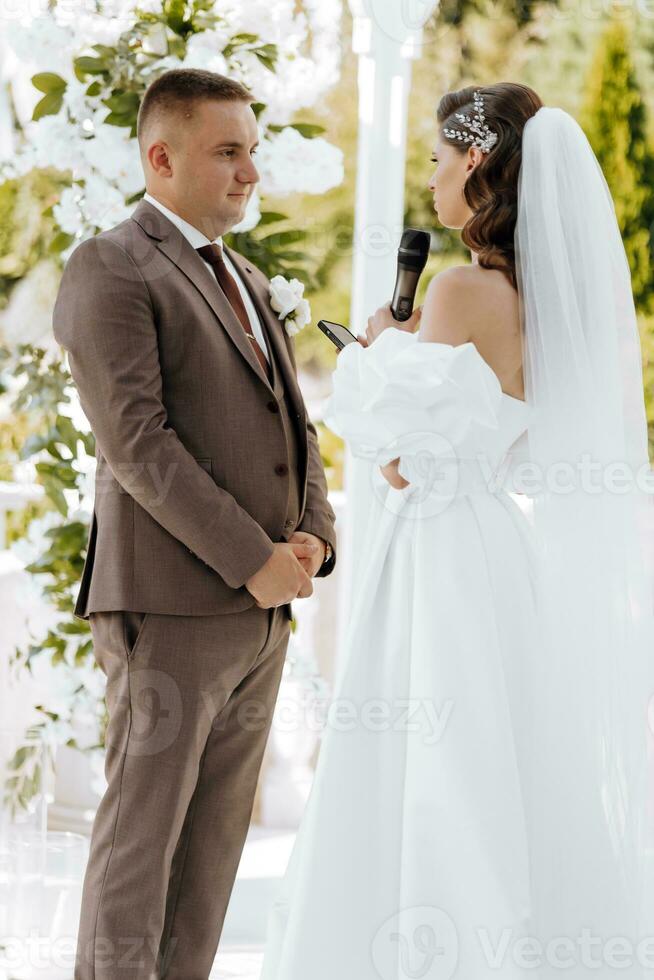 sensible ceremonia de el novia y novio. un contento recién casado Pareja es en pie en contra el antecedentes de un Boda arco, ella dice si a a él. Boda votos el emocional parte de el Boda foto