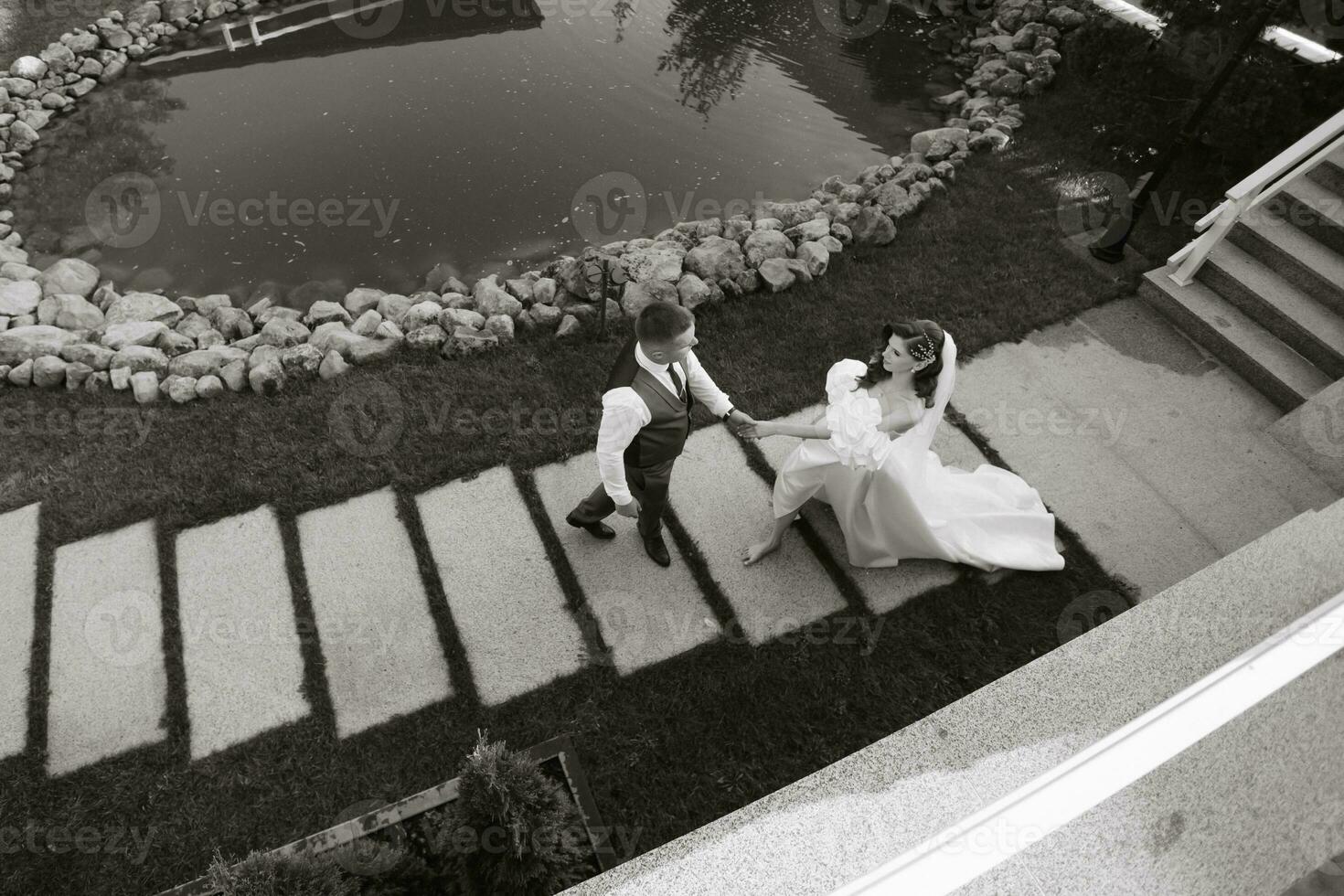 el novia y novio son caminando después el Boda ceremonia en un hermosa lugar. negro y blanco foto desde arriba. contento novia en un largo Boda vestido. Boda día.