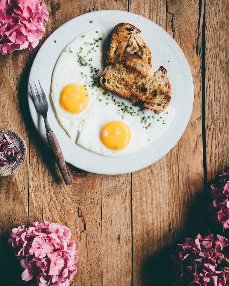 Breakfast with fried eggs, toast and flowers on a wooden background photo