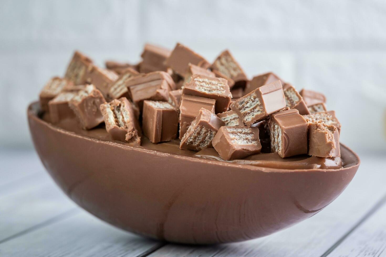 Chocolate candies in bowl on white wooden table, closeup photo