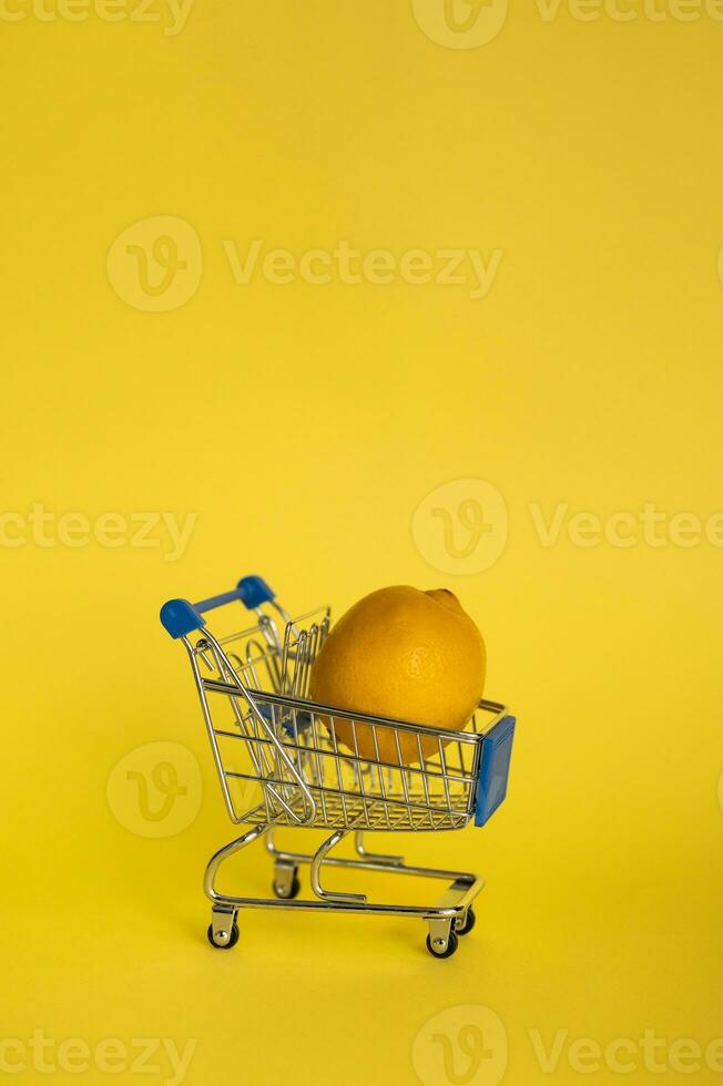 Lemon in a shopping cart on a yellow background. The concept of the sale of fruits and vegetables. photo