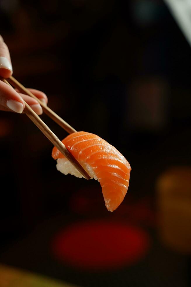 Salmon sushi with chopsticks in hand on a dark background. photo