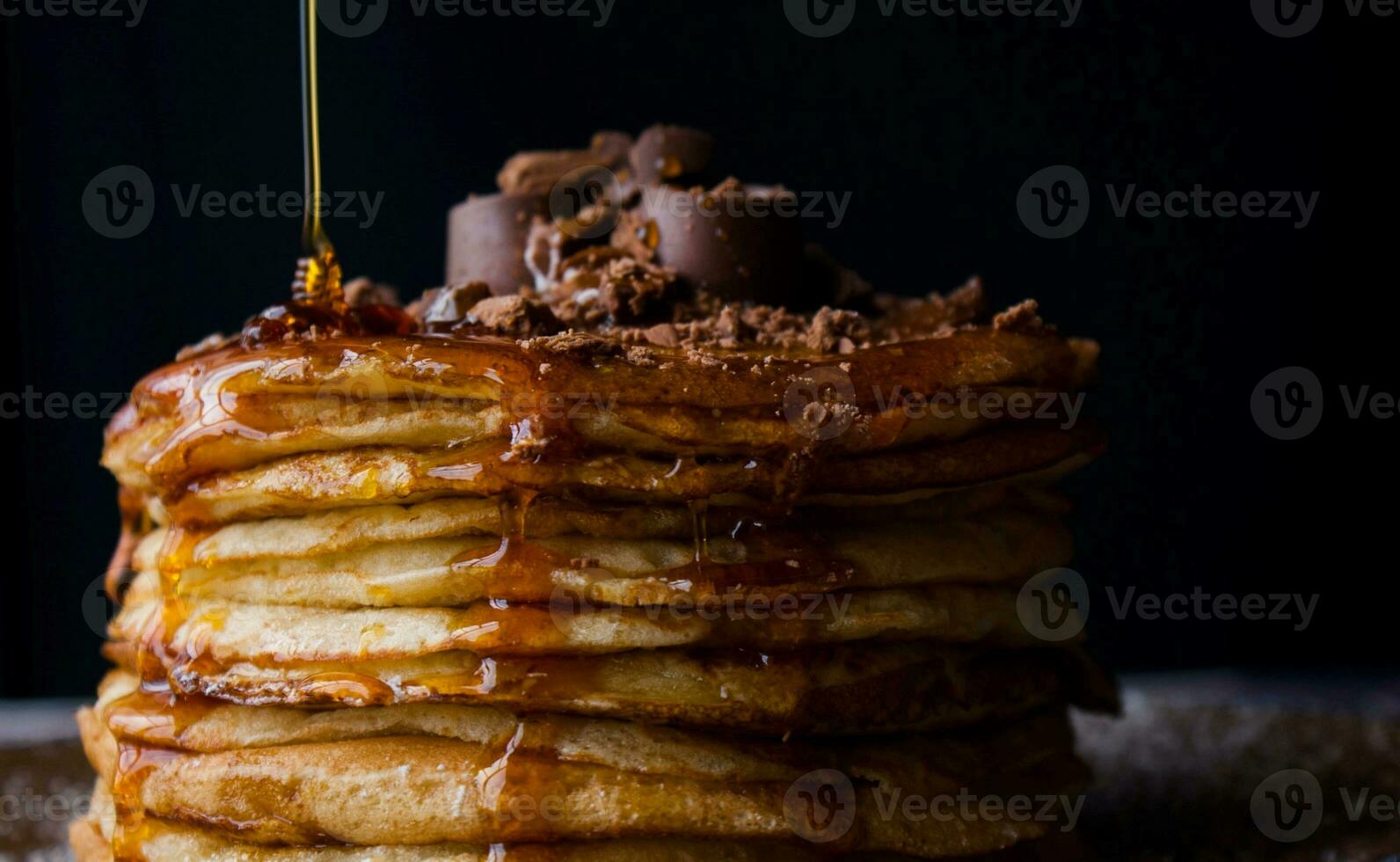 Stack of pancakes with chocolate and caramel on black background, closeup photo