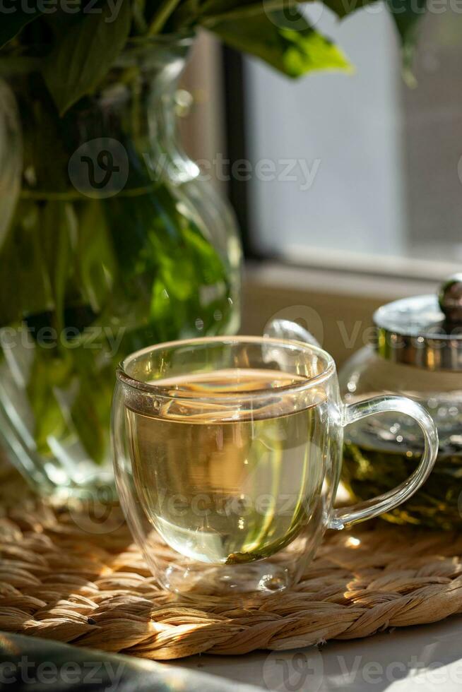 Green tea in a glass cup and teapot on the windowsill photo