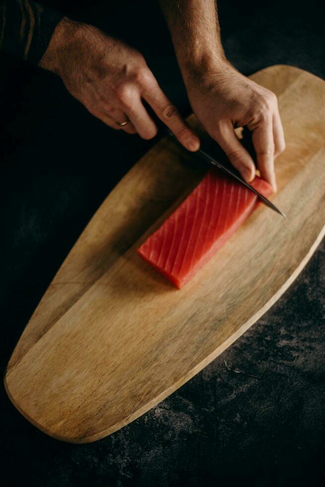 Close-up of a man's hand cutting tuna fish on a wooden cutting board photo