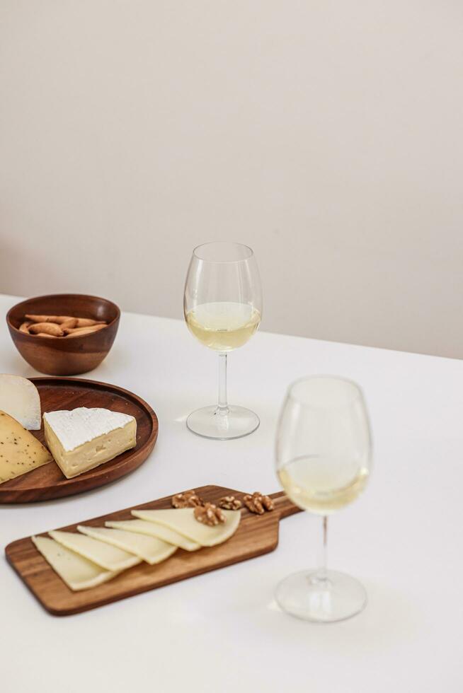 two glasses of white wine, cheese and crackers on white table photo