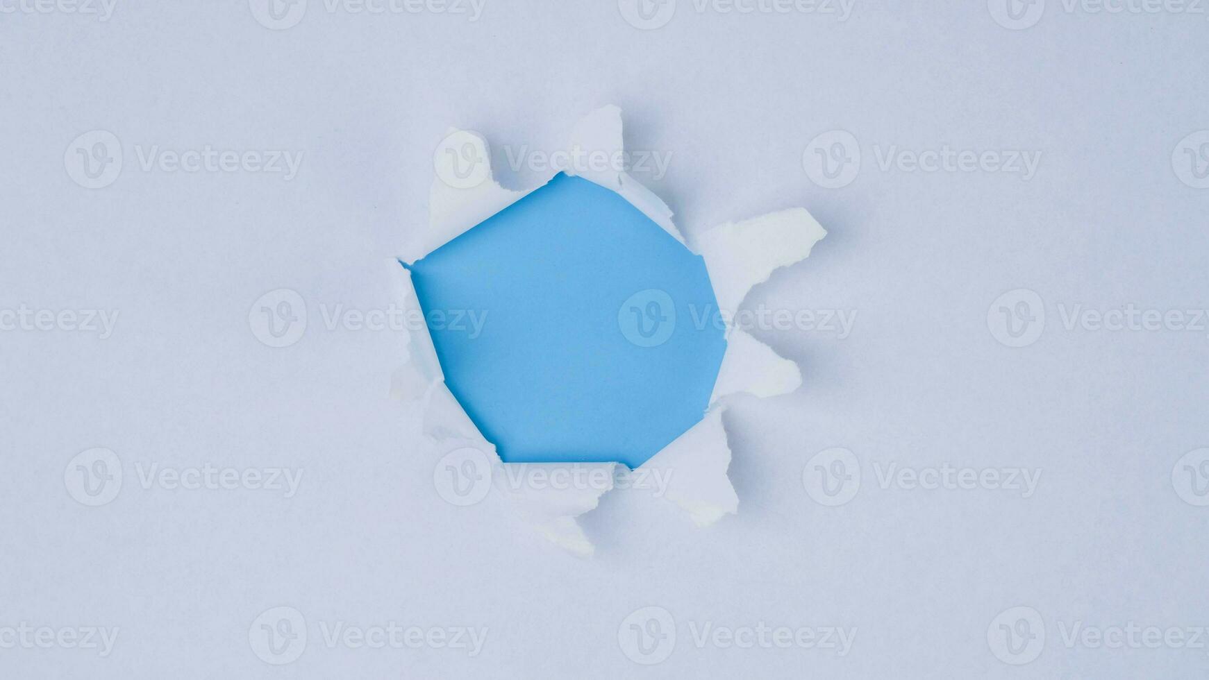 A piece of paper torn from the center revealing a blue background. photo