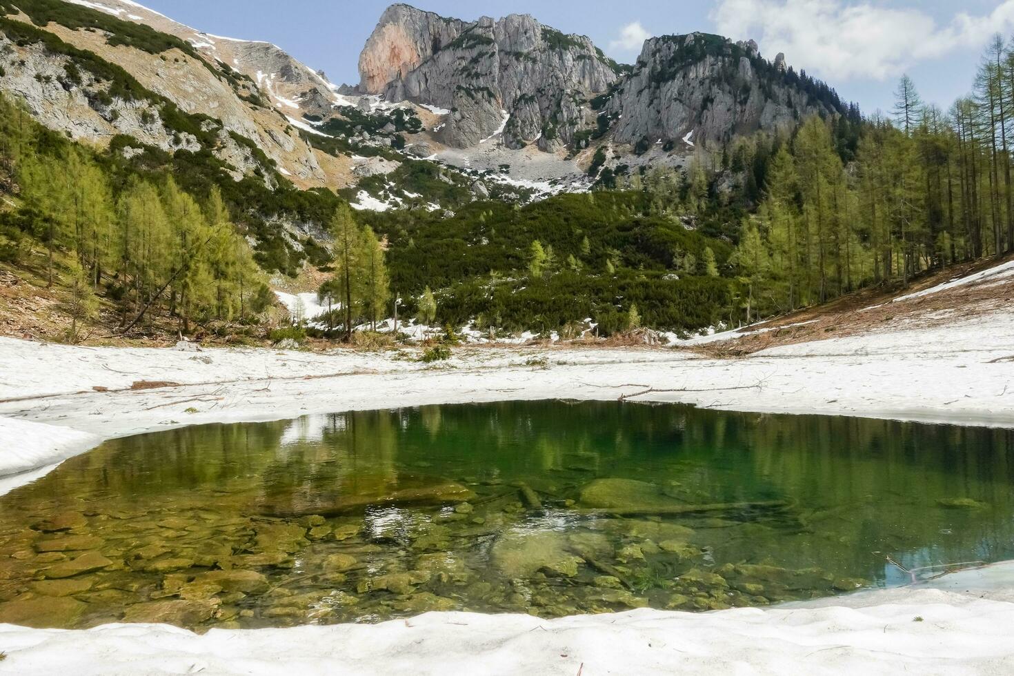 cold little lake and snow on the edge with high mountains in the background in austria photo