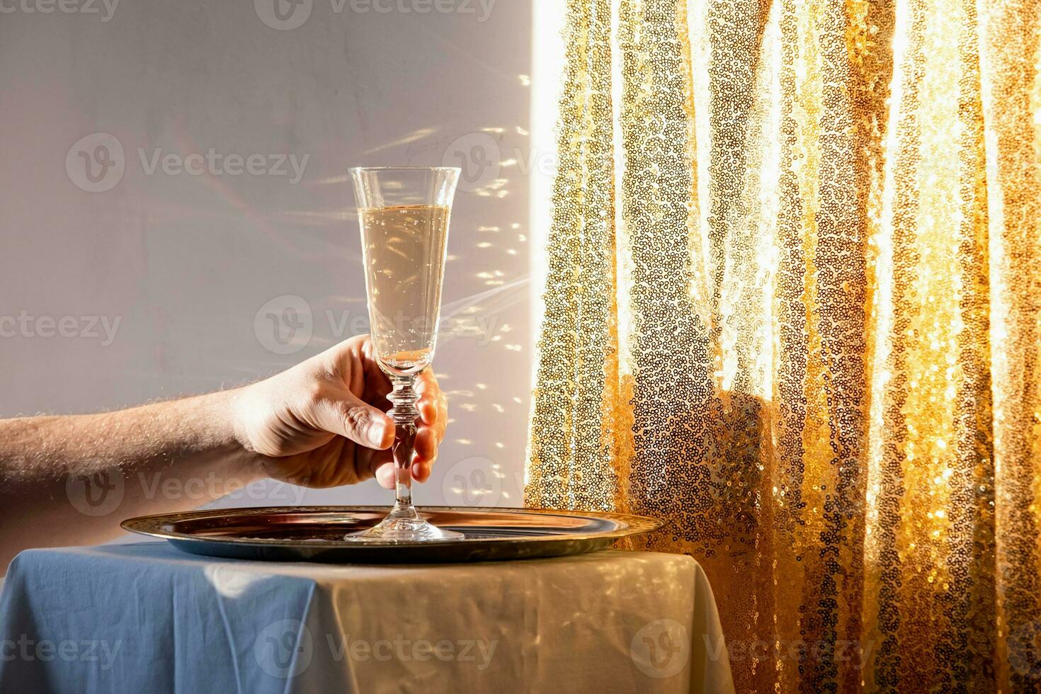 hand holding Champagne flute in tray on table against gold sparkling background photo