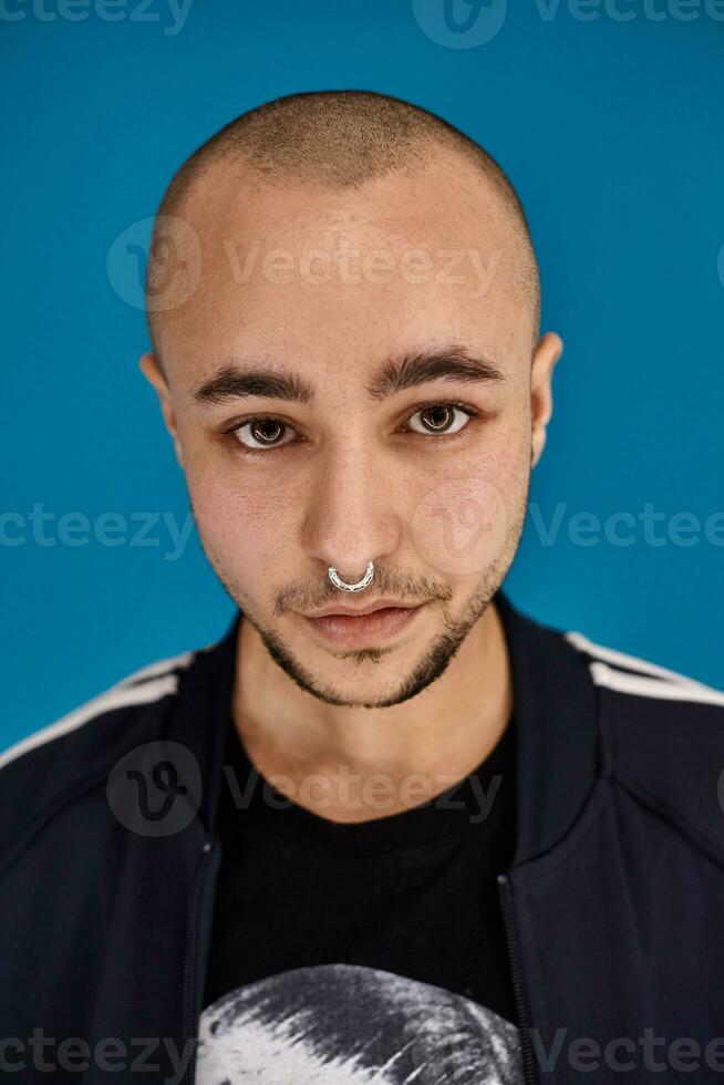 Studio shot of a young tattoed bald man posing against a blue background. 90s style. photo