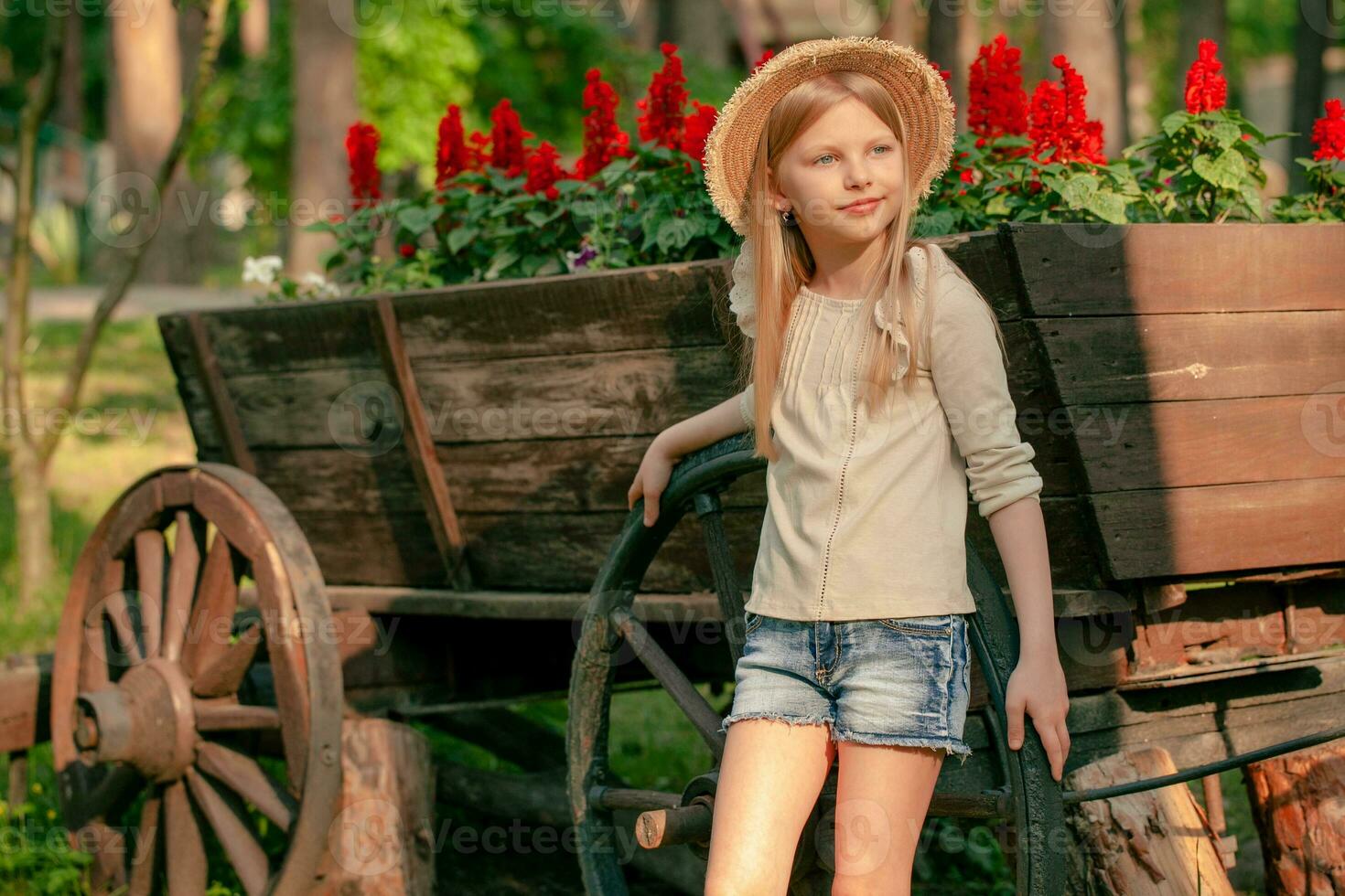 Happy tween girl posing near flower bed in shape of vintage wooden cart in park photo