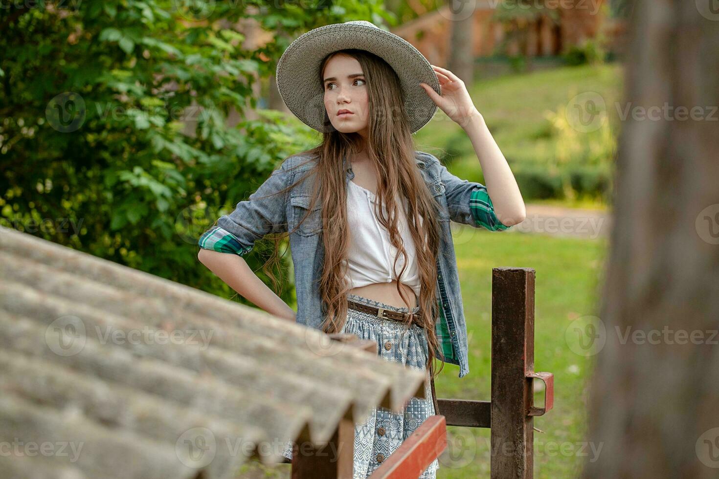 Adolescente morena en país estilo ropa en pie en verde patio interior de país casa foto
